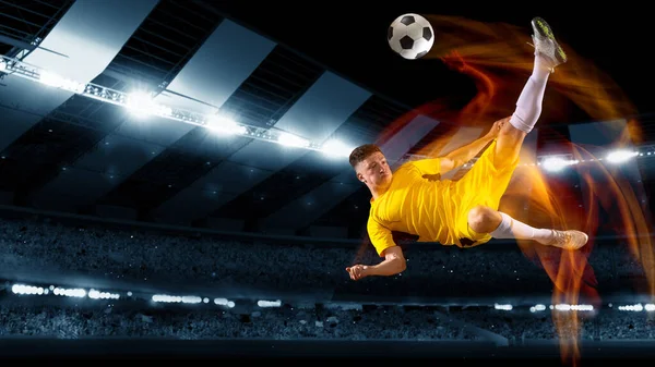 Aktivní profesionální fotbal, fotbalista kopnout míč ve skoku na tmavém nočním stadionu s baterkami. Sport, soutěž, mistrovství — Stock fotografie
