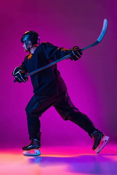Portrait of active man, professional hockey player in motion, training isolated over pink background in neon light. Side view