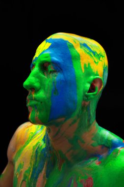 Yüzü ve omuzları siyah arkaplan üzerine izole edilmiş kalın renkli boyalı bir adamın yakın plan portresi.