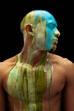 Siyah arka planda izole edilmiş koyu yeşil ve mavi boya kaplı genç kaslı adamın portresi.