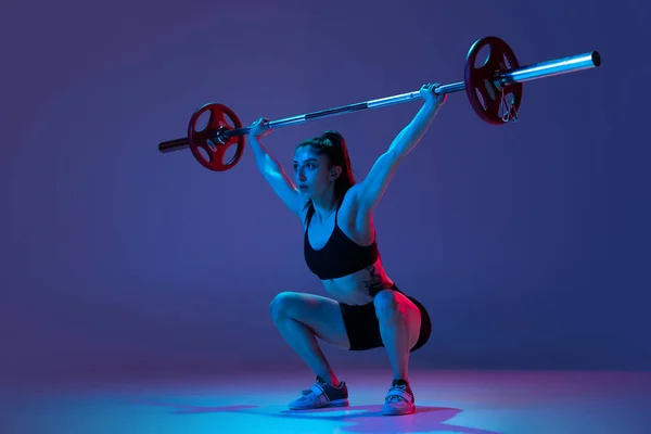Spor giyim eğitiminde kaslı bir kadının portresi. Mor arka planda, neon ışıkta izole edilmiş bir halterle. Spor, halter konsepti — Stok fotoğraf