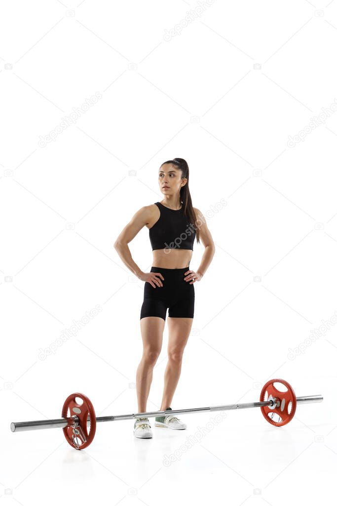 Full length portrait of muscled woman in sportswear exercising with a weight, barbell isolated on white background. Sport, weightlifting concept