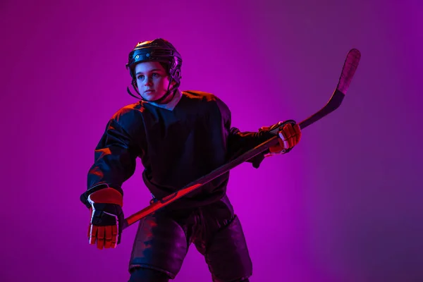 Portrait of boy, child, hockey player in protective uniform isolated over purple studio background in neon light — Stok Foto