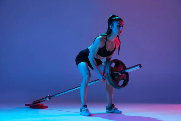Στιγμιότυπο του στούντιο της αθλήτριας, αθλητική γυναίκα ποζάρουν με barbell απομονώνονται σε μωβ φόντο σε νέον φως. Αθλητισμός, ομορφιά, έννοια της δύναμης — Φωτογραφία Αρχείου