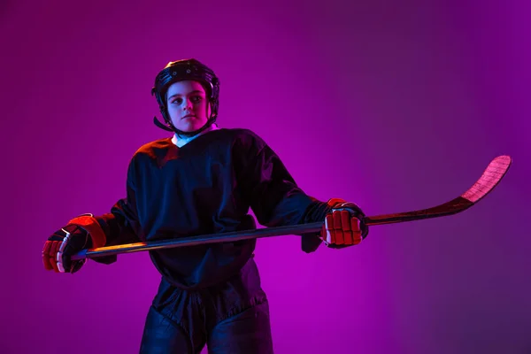 Half-length portrait of boy, child in protective uniform for hockey isolated over purple studio background in neon light — ストック写真