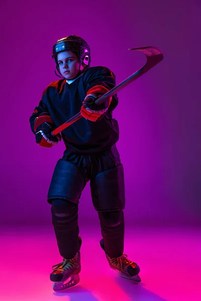 Retrato de menino, criança, jogador de hóquei em uniforme especial posando com vara isolada sobre fundo roxo em luz de néon. Infância lúdica — Fotografia de Stock