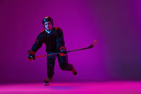 Portrait of boy, child hockey player training isolated over purple background in neon. — ストック写真