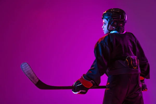 Side view portrait of little boy, child training hockey, posing isolated over purple background in neon light — ストック写真