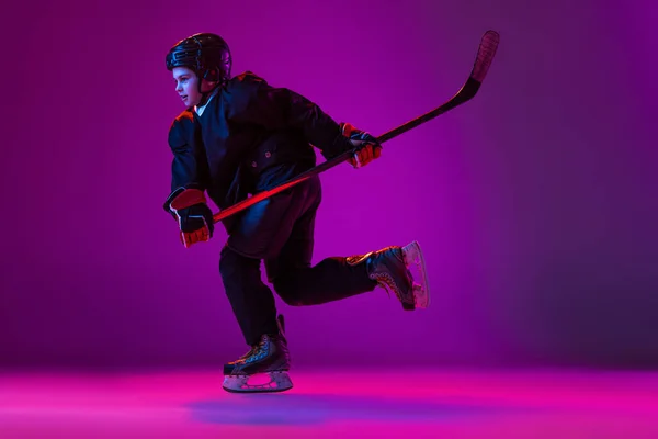 Portrait of child. hockey player training isolated over purple background in neon light. Childhood hobby — ストック写真