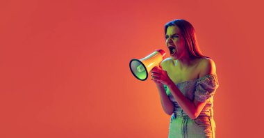 Güzel heyecanlı kız megafona bağırıyor şeftali rengi arka planda, neon ışıkta, filtrede. Duygu kavramı, müzik, haber, bilgi