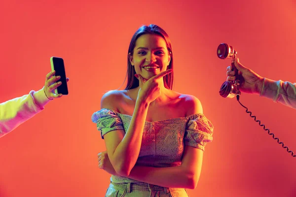 네온에 있는 산호 색깔 배경에 고립되어 있는, 현대식 전화와 역 전화 사이를 오가는 행복 한 젊은 소녀. 감정의 개념, 디지털 기술, 빈티지 패션 — 스톡 사진