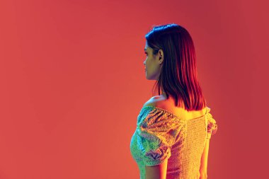 Arkadan bak. Uzun parlak saçlı güzel bir kızın portresi şeftali rengi arka planda neon filtrede izole edilmiş. Duyguların kavramı, güzellik, moda, gençlik.