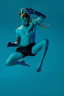 Mavi stüdyo arka planında izole edilmiş profesyonel Tayland boksörünün dinamik portresi. Spor, Muay Thai, yarışma, dövüş kulübü konsepti