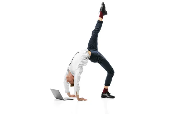 Retrato creativo del joven hombre flexible haciendo backbend y escribiendo en el ordenador portátil aislado sobre fondo de estudio blanco. Negocios en la vida moderna concepto — Foto de Stock