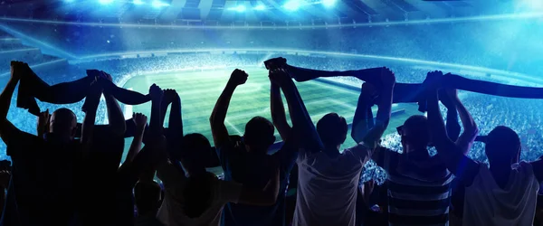 Vista posterior del fútbol, los aficionados al fútbol animando a su equipo con banderas estatales y bufandas en el estadio lleno de gente en la hora de la noche. Concepto de deporte, apoyo, competencia. Efecto fuera de foco — Foto de Stock