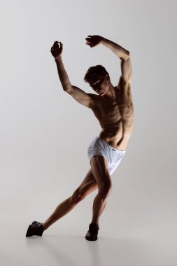 Düşünce dansı, performans. Gri arka planda yalnız dans eden, iç çamaşırlı, esnek, genç bir adam. Sanat, müzik, güzellik. Sağlıklı yaşam tarzı kavramı