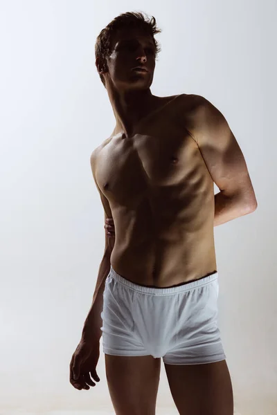 Close-up portret van jonge knappe shirtloze gespierde man met witte boxershort op grijze achtergrond. Natuurlijke schoonheid van het mannelijke lichaam — Stockfoto