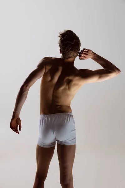 Achteraanzicht van jonge shirtloze gespierde man met witte boxershort op grijze achtergrond. Natuurlijke schoonheid van het mannelijke lichaam — Stockfoto