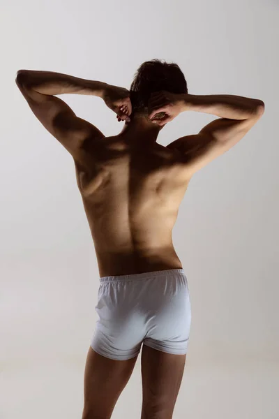 Achteraanzicht van jonge shirtloze gespierde man met witte boxershort op grijze achtergrond. Natuurlijke schoonheid van het mannelijke lichaam — Stockfoto