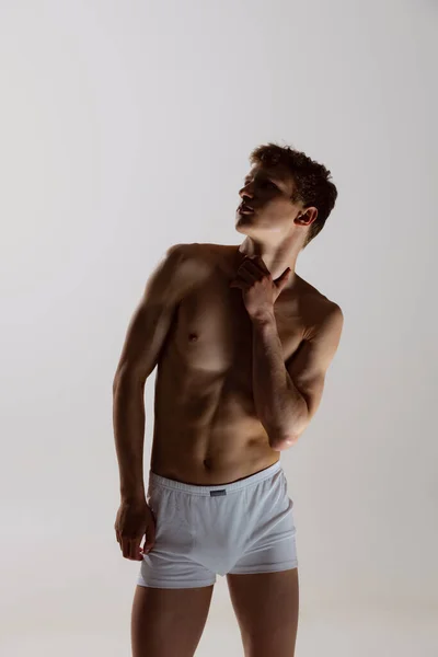 Silhouette of young shirtless muscled man wearing white boxer-briefs standing isolated on gray background. Natural beauty of male body. Emotions, love, care — ストック写真