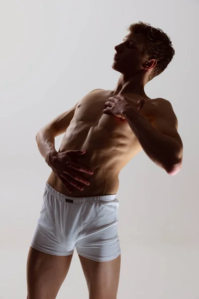 Close-up portrait of young handsome shirtless muscled man wearing white boxer-briefs standing isolated on gray background. Natural beauty of male body — Stock Photo, Image