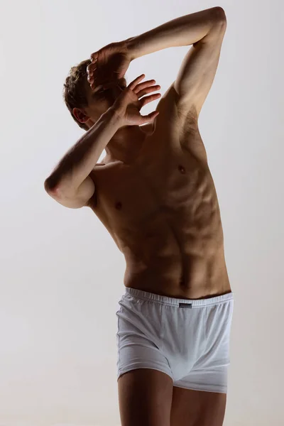 Ritratto ravvicinato di un giovane uomo muscoloso senza maglietta che indossa boxer-slip bianchi in piedi isolato su sfondo grigio. Bellezza naturale del corpo maschile — Foto Stock
