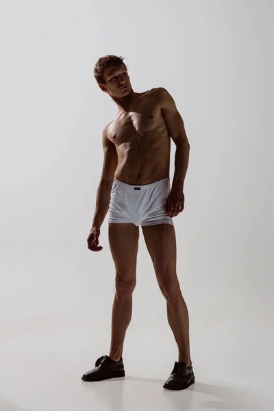 Das Ganzkörperporträt eines jungen gutaussehenden, sportlichen Mannes ohne Hemd, der einen weißen Boxershort trägt, bewegt sich sanft isoliert auf weißem Hintergrund. Wellness, Fitness, Schönheitskonzept. — Stockfoto