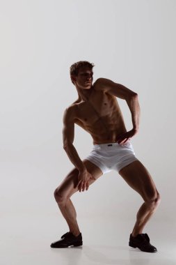 Beyaz boxer don giyen genç, üstsüz, sportif bir adamın tam boy portresi beyaz arka planda rahat bir şekilde izole edilir. Sağlık, sağlık, güzellik konsepti..