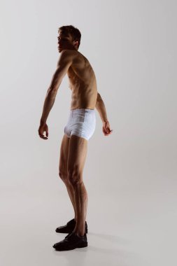 Beyaz boxer don giyen genç, üstsüz, sportif bir adamın tam boy portresi beyaz arka planda rahat bir şekilde izole edilir. Sağlık, sağlık, güzellik konsepti..