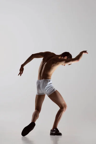 Baile temporal, actuación. Joven hombre sin camisa flexible en ropa interior bailando aislado sobre fondo gris. Arte, música, belleza. concepto de estilo de vida saludable — Foto de Stock