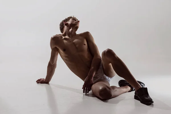 年轻英俊、无上衣、有运动能力的男子的画像，坐在地板上，与灰色背景隔离。健康、艺术、美丽的男性美的概念. — 图库照片