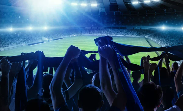 Back view of football, soccer fans cheering their team with scarfs at crowded stadium at evening time. Concept of sport, support, competition. Out of focus effect — Stock Photo, Image