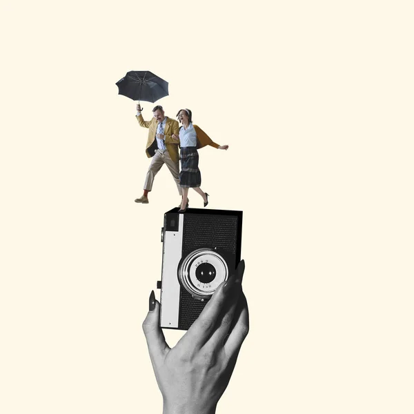 Contemporary art collage. Young loving couple with umbrella running on retro camera device isolated over light yellow background — Stock Photo, Image