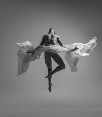 Gri stüdyo arka planında izole edilmiş kumaşla dans eden zarif kaslı erkek balerin portresi. Zarafet, sanat, güzellik konsepti. Ağırlıksız, esnek..