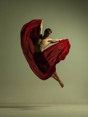 Genç kaslı bir adam, esnek bir balerin, kırmızı kumaşla çalışıyor, zeytin rengi arka planda izole edilmiş kumaş. Tiyatro, duygular, zarafet, sanat, güzellik konsepti.