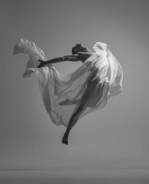 Kebebasan. Potret hitam dan putih dari penari balet pria berotot yang menari dengan kain, kain diisolasi di latar belakang studio abu-abu. Grace, seni, konsep kecantikan. — Stok Foto