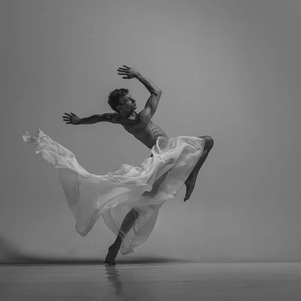 Speranza. Ritratto in bianco e nero di grazioso ballerino maschile muscoloso che balla con tessuto, tessuto isolato su sfondo grigio da studio. Grazia, arte, concetto di bellezza. Senza peso, flessibile. — Foto Stock