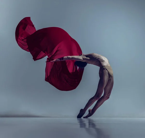 Porträt eines jungen Mannes, flexibler Balletttänzer in Aktion mit rotem Stoff, Stoff isoliert auf marineblauem Studiohintergrund. Anmut, Kunst, Schönheitskonzept. — Stockfoto