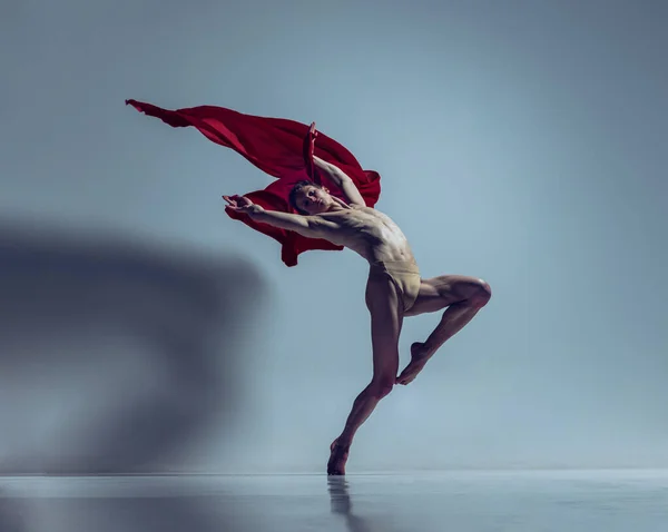 Porträt eines jungen Mannes, flexibler Balletttänzer in Aktion mit rotem Stoff, Stoff isoliert auf marineblauem Studiohintergrund. Anmut, Kunst, Schönheitskonzept. — Stockfoto