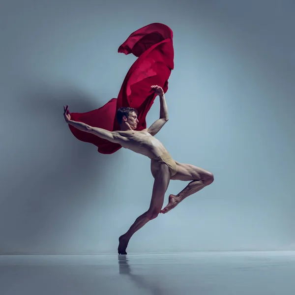 Retrato de jovem, dançarino de balé flexível em ação com tecido vermelho, pano isolado no fundo do estúdio da marinha. Graça, arte, conceito de beleza. — Fotografia de Stock