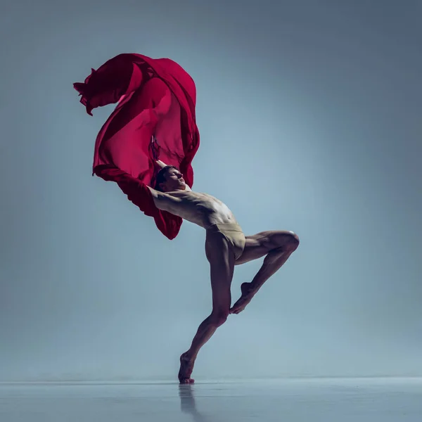 Πορτρέτο του νεαρού άνδρα, ευέλικτη χορεύτρια μπαλέτου σε δράση με κόκκινο ύφασμα, ύφασμα που απομονώνεται σε ναυτικό φόντο στούντιο. Χάρη, τέχνη, έννοια της ομορφιάς. — Φωτογραφία Αρχείου