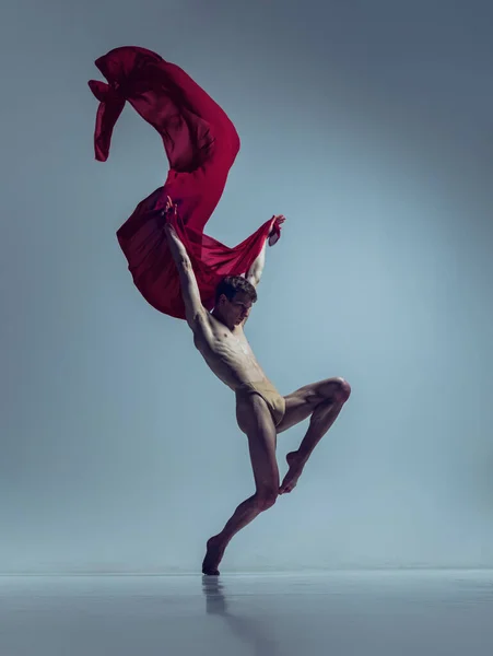 Retrato de jovem, dançarino de balé flexível em ação com tecido vermelho, pano isolado no fundo do estúdio da marinha. Graça, arte, conceito de beleza. — Fotografia de Stock