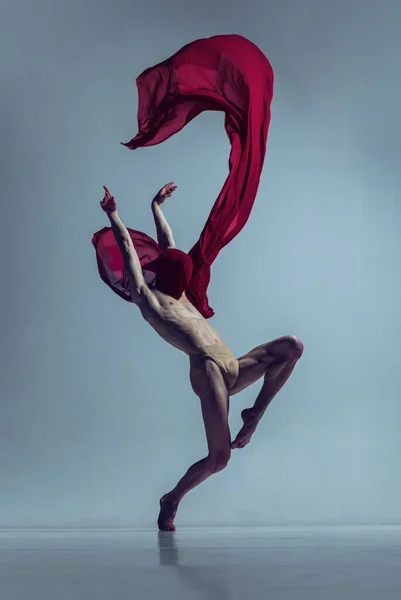 Retrato de jovem, dançarino de balé flexível em ação com tecido vermelho, pano isolado no fundo do estúdio da marinha. Graça, arte, conceito de beleza. — Fotografia de Stock