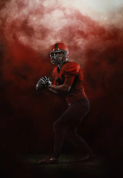 Céu vermelho. Retrato criativo do jovem, jogador de futebol americano no estádio em movimento sobre fundo fumado. Esporte, desafio, metas, atividade, conceito de vida esportiva. — Fotografia de Stock