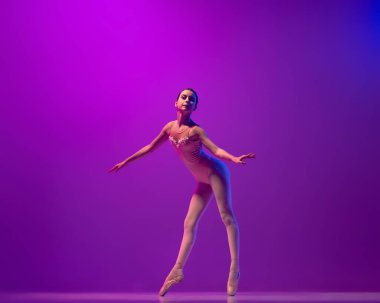 Esnek bir bayan balerin, sahne kıyafetli bir genç kız ve mor arka planda izole bir şekilde dans ediyor. Sanat, zarafet, güzellik, bale okulu konsepti