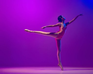 Esnek bir bayan balerin, sahne kıyafetli bir genç kız ve mor arka planda izole bir şekilde dans ediyor. Sanat, zarafet, güzellik, bale okulu konsepti