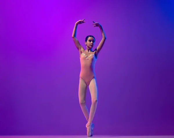 Portrait of young little ballet dancer, teen practicing, dancing isolated on purple background in neon light. Art, grace, beauty, ballet school concept — Photo