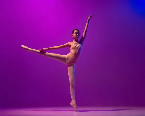Στιγμιότυπο από ένα όμορφο κορίτσι σχολικής ηλικίας, χορεύτρια μπαλέτου που χορεύει απομονωμένη σε μωβ φόντο σε νέον φως. Τέχνη, χάρη, ομορφιά, μπαλέτο έννοια σχολή — Φωτογραφία Αρχείου