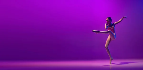 Portrait of young little ballet dancer, teen jumping isolated on purple background in neon light. Art, grace, beauty, ballet school concept — Stock Photo, Image