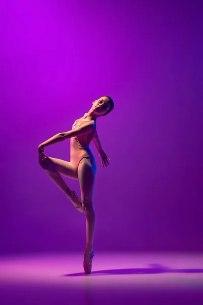 Uma dançarina de balé jovem flexível, adolescente em roupa de palco e pointes dançando isolado em fundo roxo em luz de néon. Arte, graça, beleza, conceito de escola de balé — Fotografia de Stock